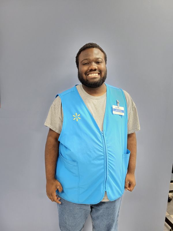 Smiling Man in a blue vest against a wall