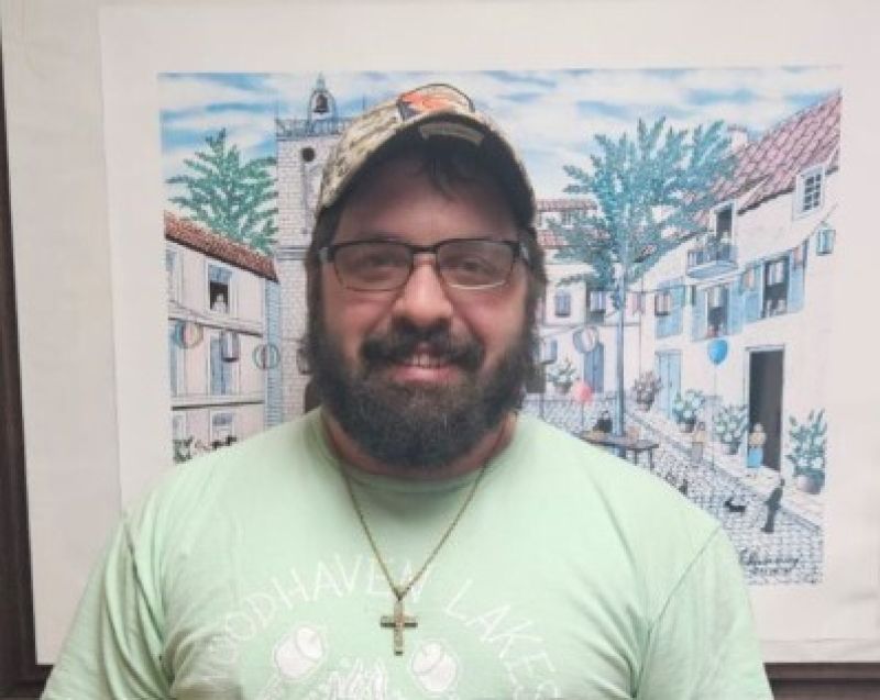 Man Smiling with a baseball cap on in a green shirt